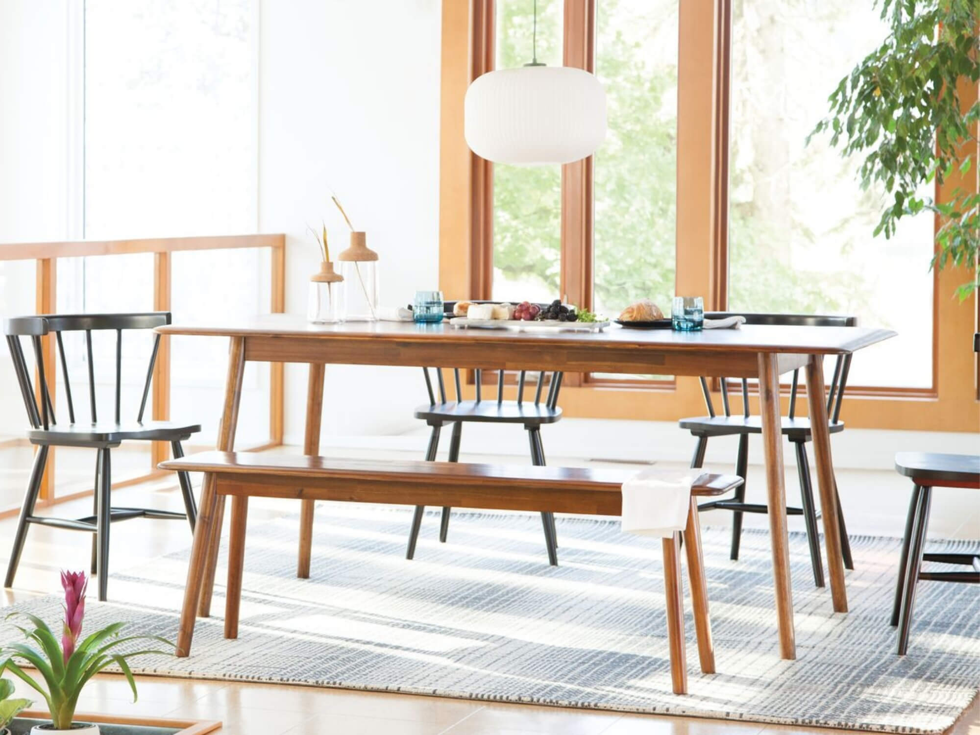 The Kacia dining bench seat and dining table in java in a bright, spacious dining room with black Lyla armchairs